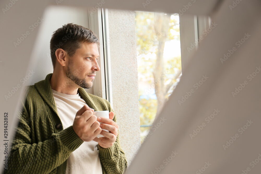Mann mit Tasse blickt aus dem Fenster